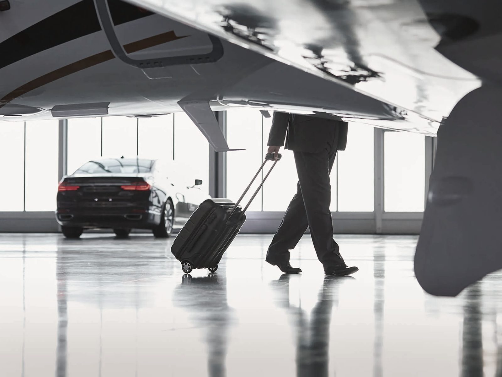 An executive crossing an apron toward a waiting car, aircraft overhead